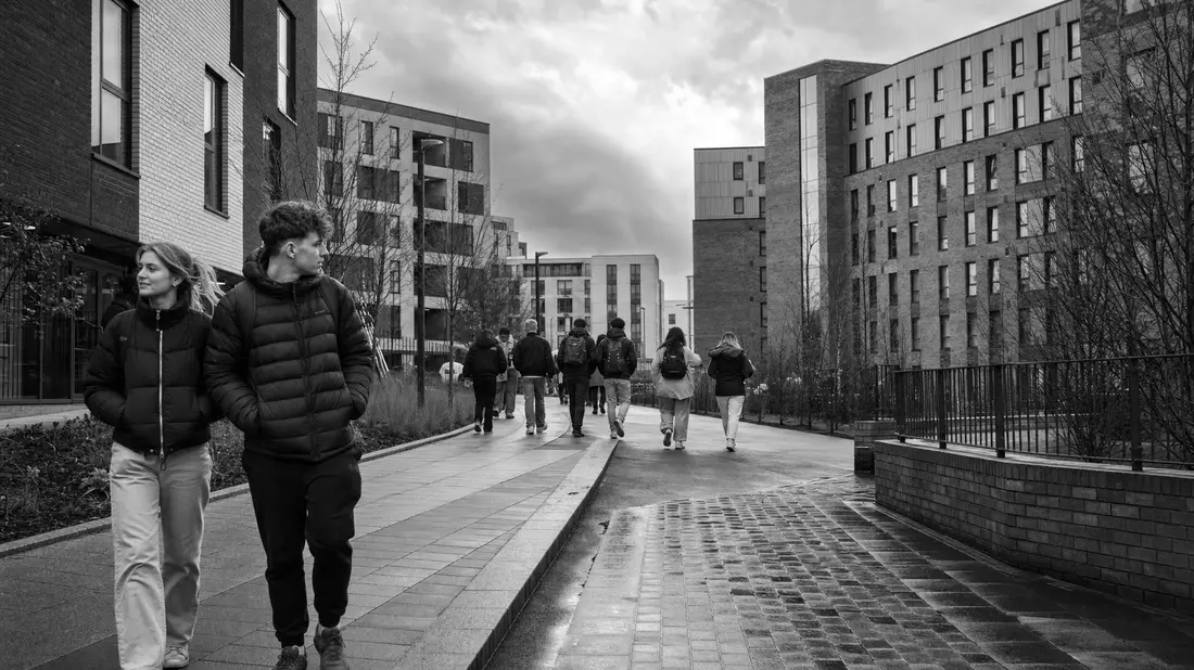 Schwarzweiß-Reportagefoto von Studierenden zwischen modernen Wohnblöcken einer Universitätsstadt