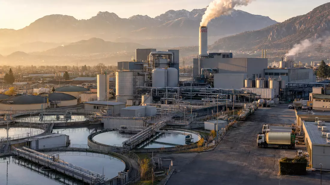 Industrieanlage mit Wassertanks und Schornstein bei Sonnenaufgang, Symbolbild für Hera S.p.A