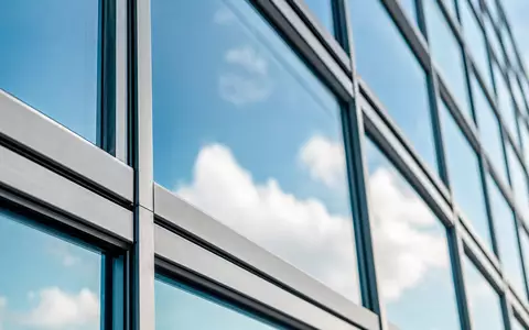Hamborner REIT DE0006013006 – Makro-Detailaufnahme einer modernen Glasfassade mit Stahlrahmen und blauer Wolkenspiegelung - Foto: THN
