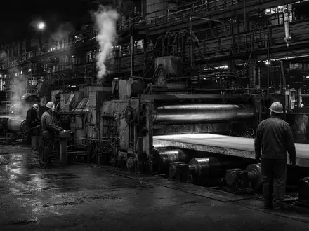 Schwarzweiße Reportage-Aufnahme dokumentiert SSAB AB, ISIN SE0000108656, mit Arbeitern an schwerer industrieller Stahlwalzanlage - Foto: THN