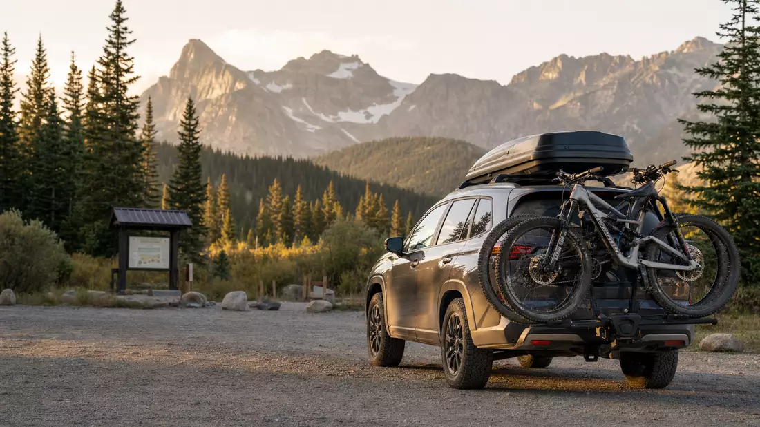 SUV mit Dachbox und Fahrradträgern vor Bergpanorama, Symbolbild Outdoor-Ausrüstung