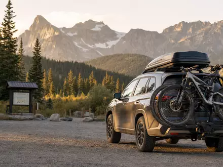Thule Group AB SE0007158910 zeigt ein SUV mit Dachbox und Fahrradträgern vor Bergkulisse - Foto: THN