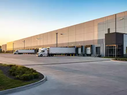 Prologis Inc. mit ISIN US74340W1036 zeigt fotorealistische moderne Logistikhalle mit Lkw an Laderampen bei Sonnenuntergang - Foto: THN
