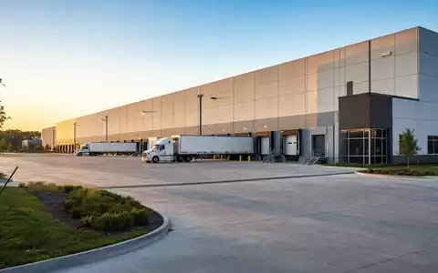 Prologis Inc. mit ISIN US74340W1036 zeigt fotorealistische moderne Logistikhalle mit Lkw an Laderampen bei Sonnenuntergang - Foto: THN