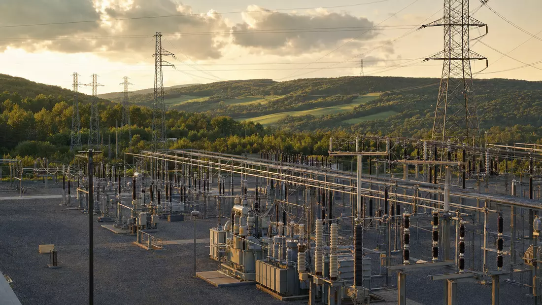 Umspannwerk mit Hochspannungsmasten in hügeliger Landschaft bei Sonnenuntergang