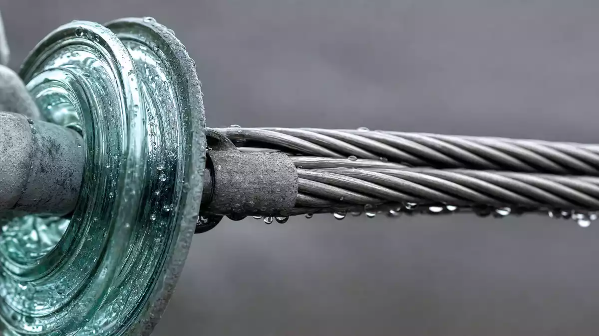 Makroaufnahme von Glasisolator und geflochtenem Stromkabel mit Wassertropfen