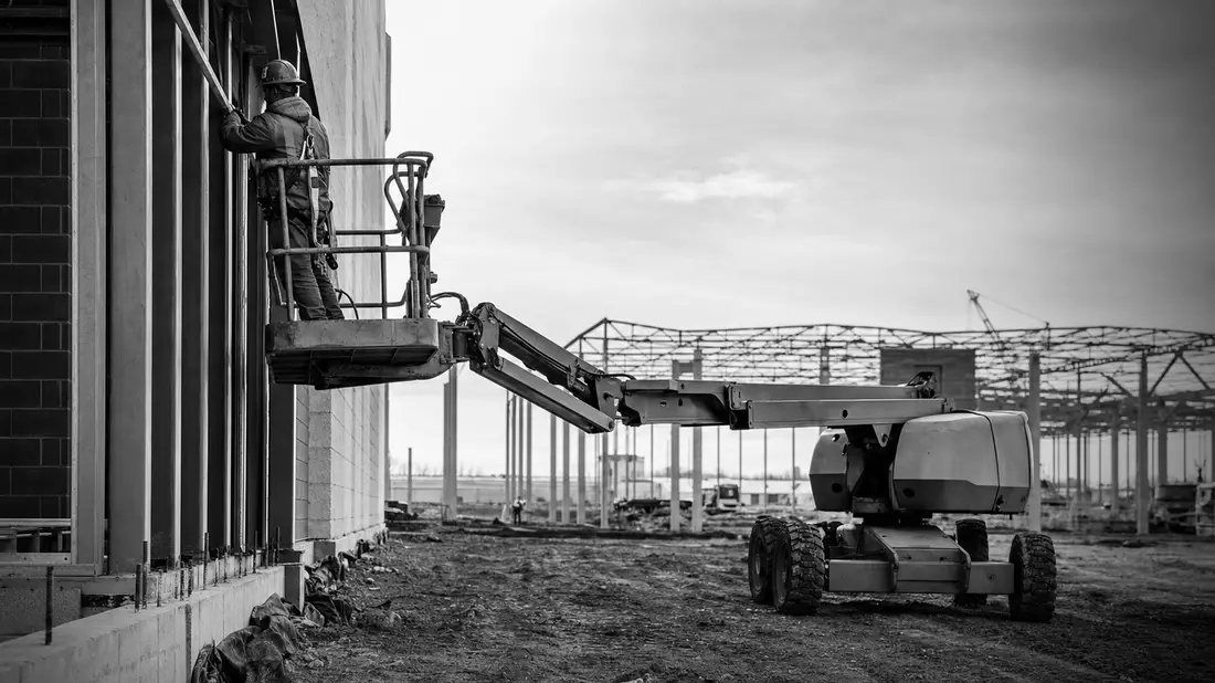 Schwarzweiß-Reportagefoto eines Arbeiters auf einer Hebebühne an einer Baustelle