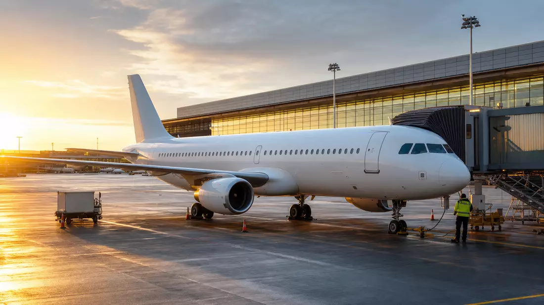Weißes unbedrucktes Passagierflugzeug am Flughafen-Gate bei Sonnenuntergang