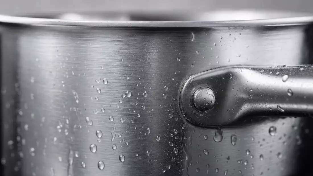 Makroaufnahme einer gebürsteten Edelstahl-Topfoberfläche mit Wassertropfen