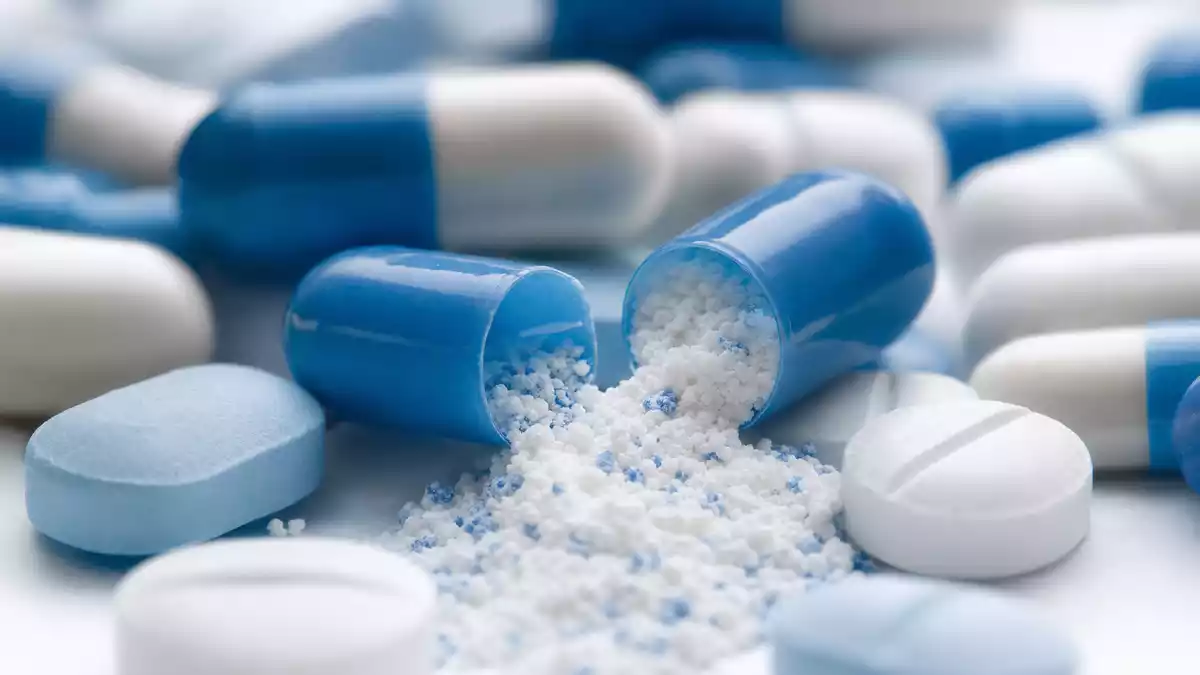Makrofotografie blauer Pharma-Kapseln mit freigesetztem Pulver auf weißem Untergrund