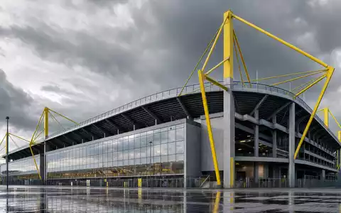 Borussia Dortmund DE0005493092 Architektur Render des modernen Stadiongebäudes mit gelben Stahlmasten bei bewölktem Himmel - Foto: THN
