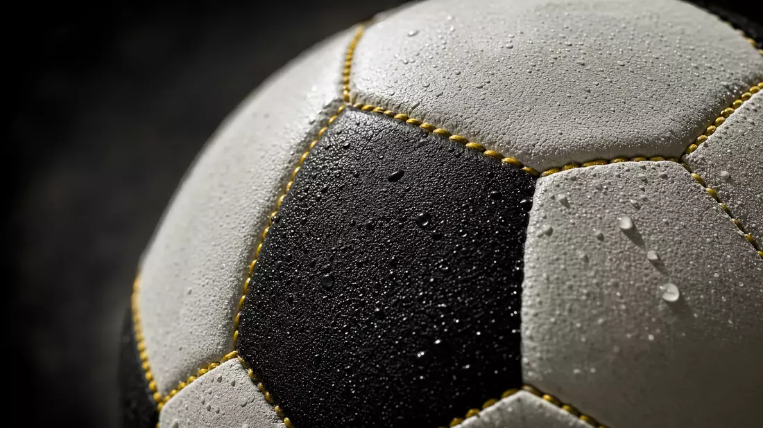Extreme Makroaufnahme der schwarz-weißen Lederoberfläche eines Fußballs mit gelben Nähten