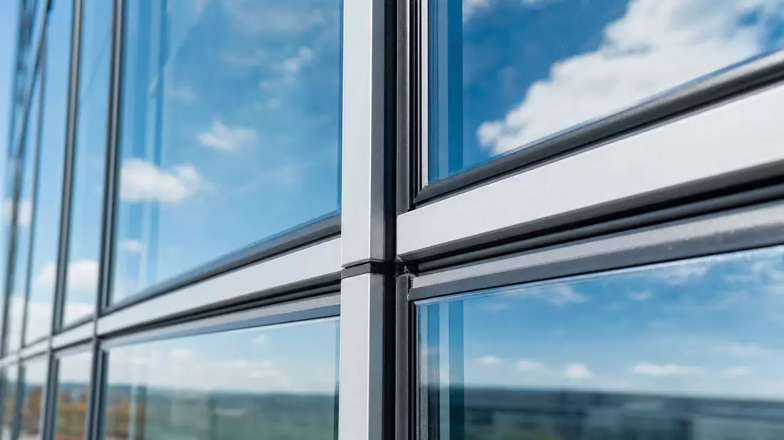 Makro-Nahaufnahme einer Glasvorhangfassade mit Aluminium-Pfosten-Riegel-Konstruktion und Wolkenreflexion