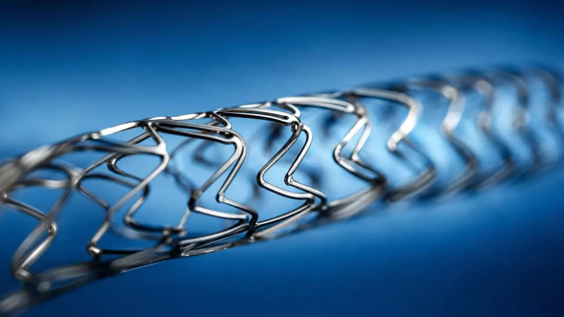 Extreme Makroaufnahme eines metallischen Koronarstents mit Nitinol-Gitterstruktur auf blauem Hintergrund