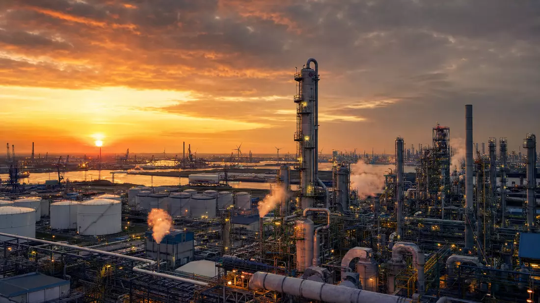 Industrielle Chemieanlage mit Türmen und Dampf bei Sonnenuntergang am Hafen