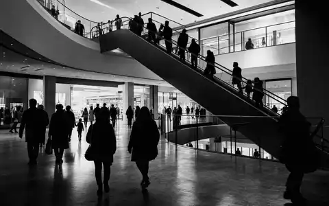 Deutsche EuroShop DE0007480204 – Dokumentarische Schwarzweiß-Aufnahme von Besuchern auf Rolltreppen im Einkaufszentrum - Foto: THN