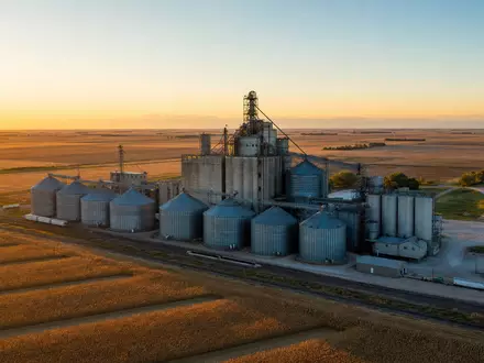 Archer-Daniels-Midland US0394831020 betreibt riesige Getreidesilos inmitten goldener Maisfelder bei warmem Sonnenuntergang in der Midwest-Region - Foto: THN