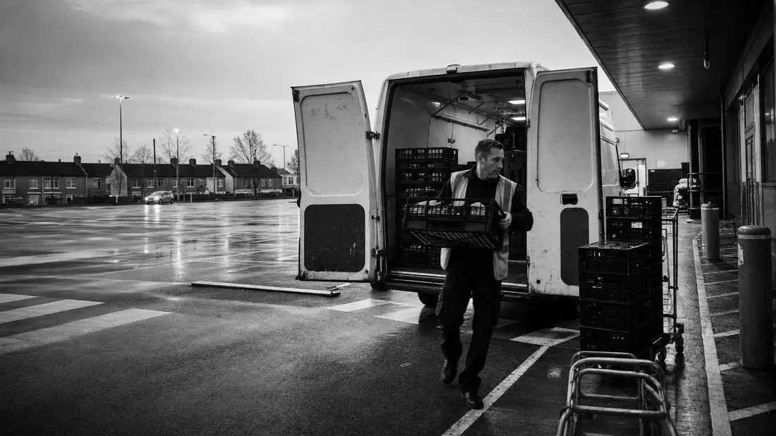 Schwarzweiß-Reportagefoto eines Lieferwagens beim Entladen an einer Supermarkt-Rampe
