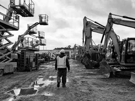 Schwarzweiß-Reportage dokumentiert Ashtead Group plc, ISIN GB0000533728, Baumaschinen-Vermieter auf schlammiger amerikanischer Großbaustelle mit Arbeiter - Foto: THN
