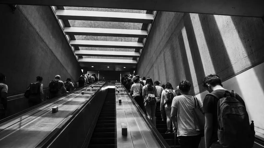 Schwarzweiß-Reportagefoto einer belebten Rolltreppe mit Pendlern in U-Bahn-Station