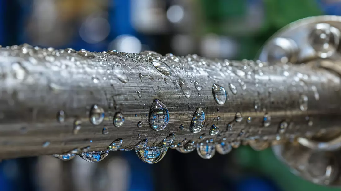 Makrofoto von Wassertropfen auf einer metallischen Rohrleitung mit Lichtreflexen