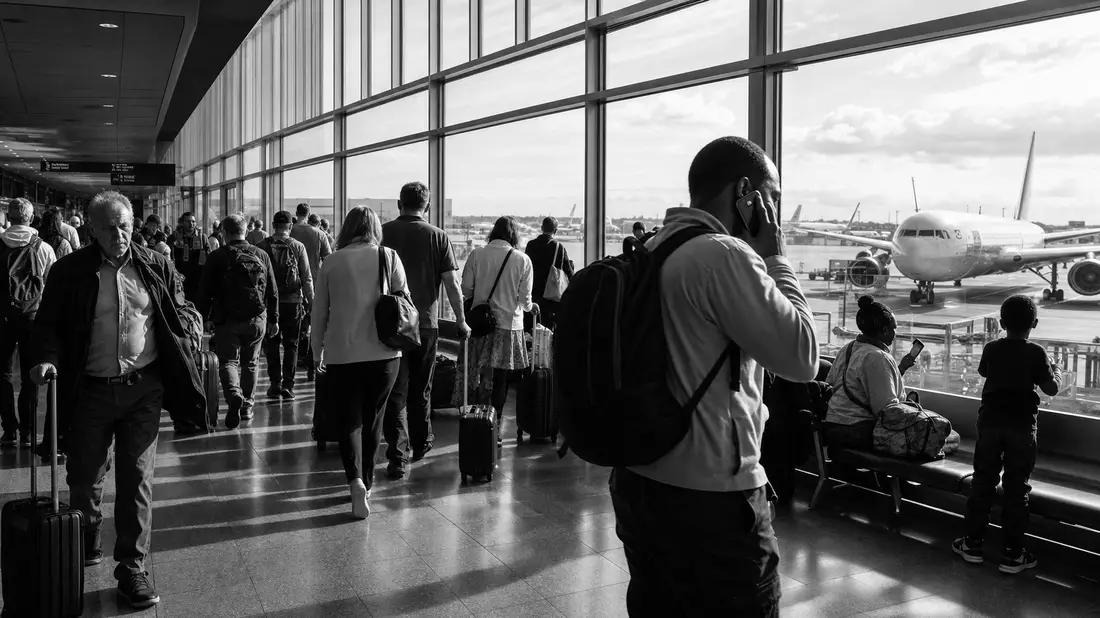 Schwarzweiß-Reportagefoto von Reisenden im Flughafenterminal mit Flugzeugblick