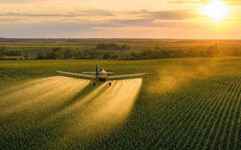 FMC Corp. Pflanzenschutz-Flugzeug sprüht Insektizid über grüne Maisfelder bei goldenem Licht ISIN US3024913036 - Foto: THN