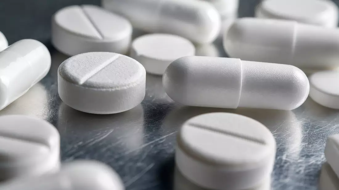 Makroaufnahme weißer Tabletten und Kapseln auf reflektierender Stahloberfläche