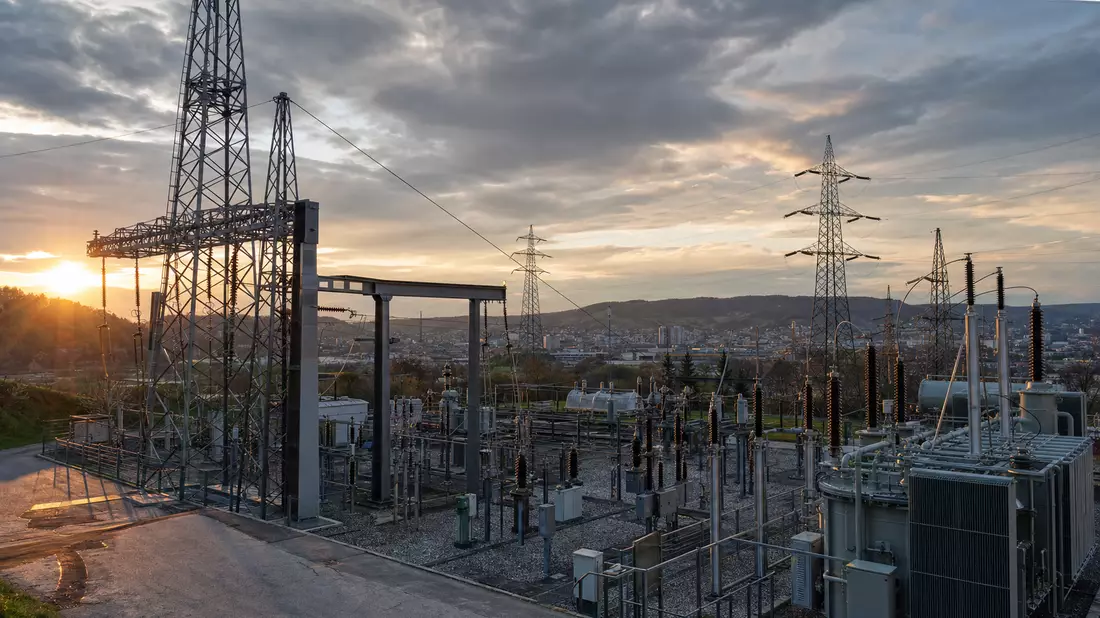 Umspannwerk mit Hochspannungsmasten und Transformatoren im Abendlicht
