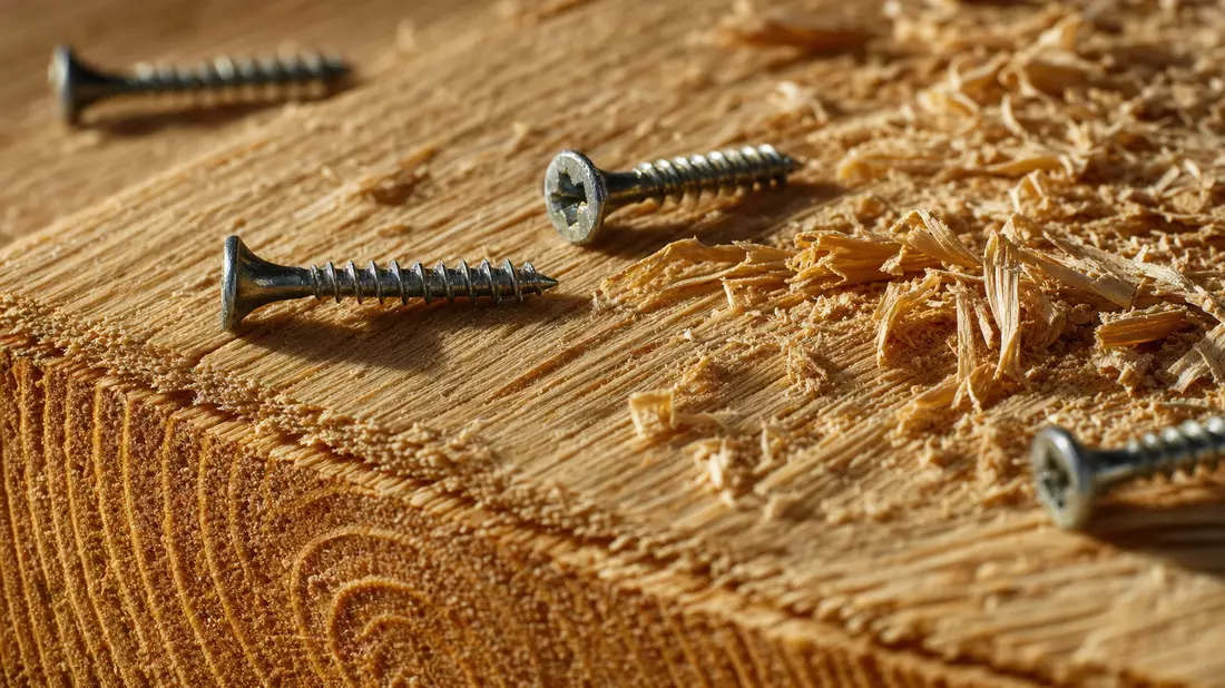 Makrofoto von Holzmaserung mit Schrauben und Holzspänen im warmen Streiflicht