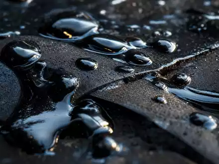 Marathon Oil (US5658491064): Makroaufnahme glänzender Rohöltropfen auf dunklem Metall zeigt die zähflüssige Textur des Erdöls - Foto: THN