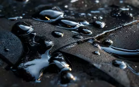 Marathon Oil (US5658491064): Makroaufnahme glänzender Rohöltropfen auf dunklem Metall zeigt die zähflüssige Textur des Erdöls - Foto: THN