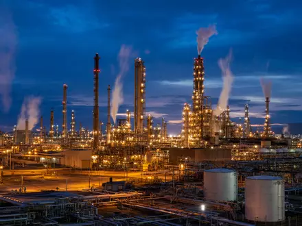 Marathon Petroleum US56585A1025 zeigt eine hell beleuchtete Erdölraffinerie mit hohen Türmen bei Abenddämmerung und Dampf - Foto: THN