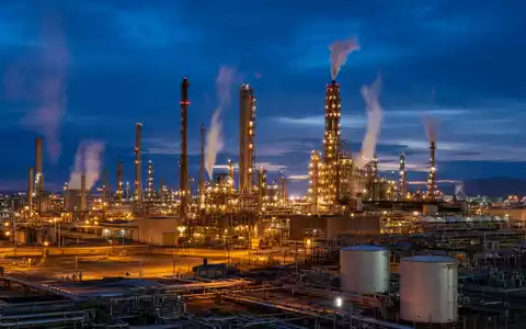 Marathon Petroleum US56585A1025 zeigt eine hell beleuchtete Erdölraffinerie mit hohen Türmen bei Abenddämmerung und Dampf - Foto: THN