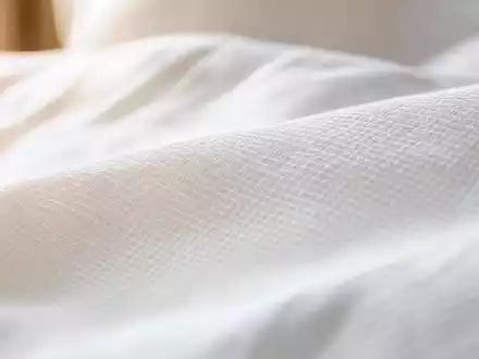 Marriott International US5719032022 zeigt Makroaufnahme von feiner Bettwäsche-Textur mit warmem seitlichem Lichteinfall - Foto: THN