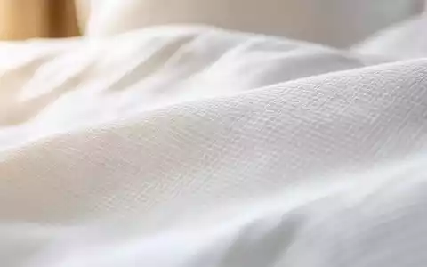 Marriott International US5719032022 zeigt Makroaufnahme von feiner Bettwäsche-Textur mit warmem seitlichem Lichteinfall - Foto: THN