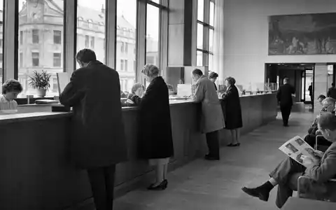 Schwarzweiß-Reportagefoto einer belebten Bankfiliale, passend zu Danske Bank A/S, ISIN DK0010274414, im dokumentarischen Stil - Foto: THN