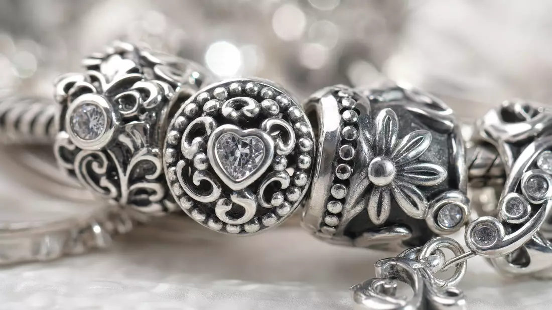 Makrofoto eines gravierten Silber-Charm-Armbands mit funkelnden Edelsteinen im Detail