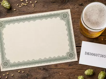 Flatlay-Arrangement kombiniert Royal Unibrew A/S, ISIN DK0060738599, mit Aktienzertifikat, ISIN-Karte und Bierglas auf Holztisch - Foto: THN