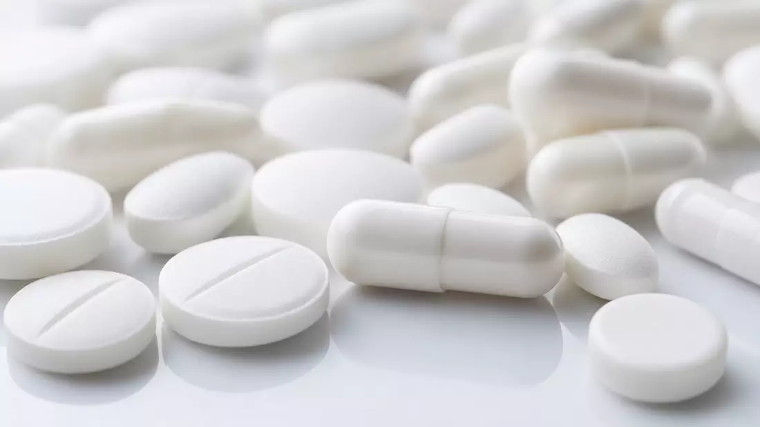 Nahaufnahme von weißen Tabletten und Kapseln auf glatter Oberfläche