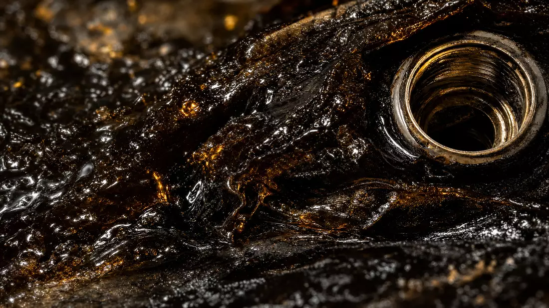 Makroaufnahme von glänzendem schwarzem Bitumen mit metallischem Ventilgewinde
