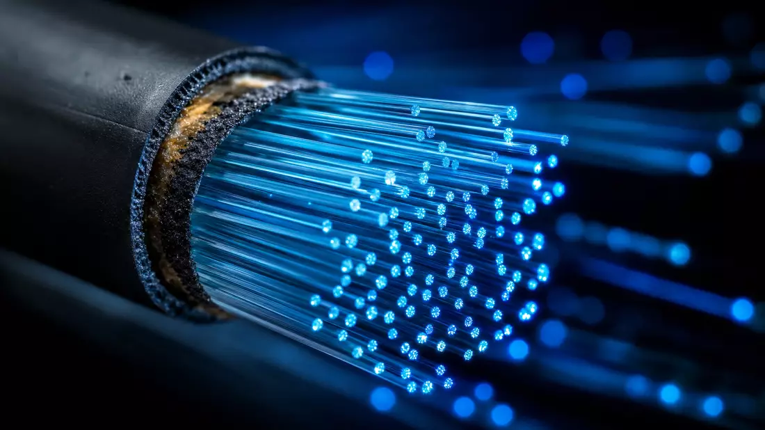Extreme Makroaufnahme Glasfaserkabel mit blau leuchtenden Datensträngen und Bokeh-Hintergrund