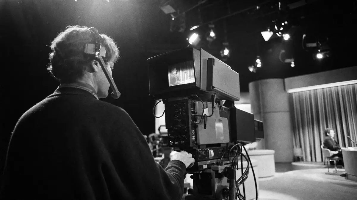 Schwarz-weißes Reportagefoto eines Kameramanns an Fernsehkamera im generischen TV-Studio
