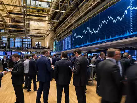 State Street Corp. (US8574771031) begleitet Editorial-Szene vom NYSE-Handelsparkett mit Kursdiagrammen im Hintergrund - Foto: THN