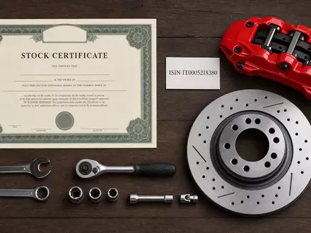 Brembo S.p.A. (ISIN IT0005218380) symbolisiert dieses Flatlay mit Aktienzertifikat, ISIN-Karte, Bremssattel und Bremsscheibe - Foto: THN