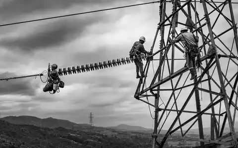 Southern Company US8425871071 dokumentiert Techniker bei Wartungsarbeiten an Hochspannungsmasten in dramatischer Schwarzweiß-Reportage-Fotografie - Foto: THN