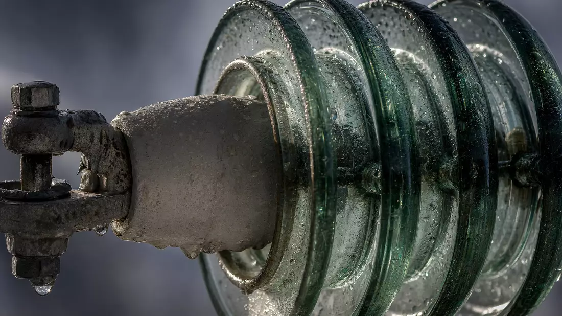 Makroaufnahme eines Glasisolators mit Wassertropfen an einer Stromleitung