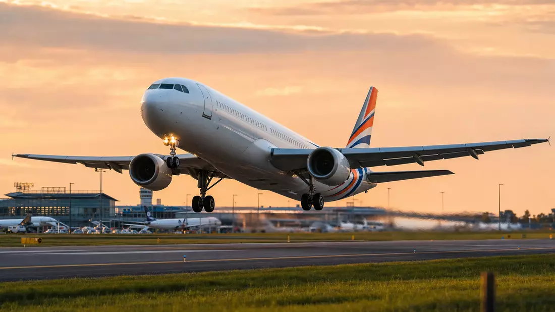 Weißes Passagierflugzeug hebt bei Sonnenuntergang von der Startbahn ab