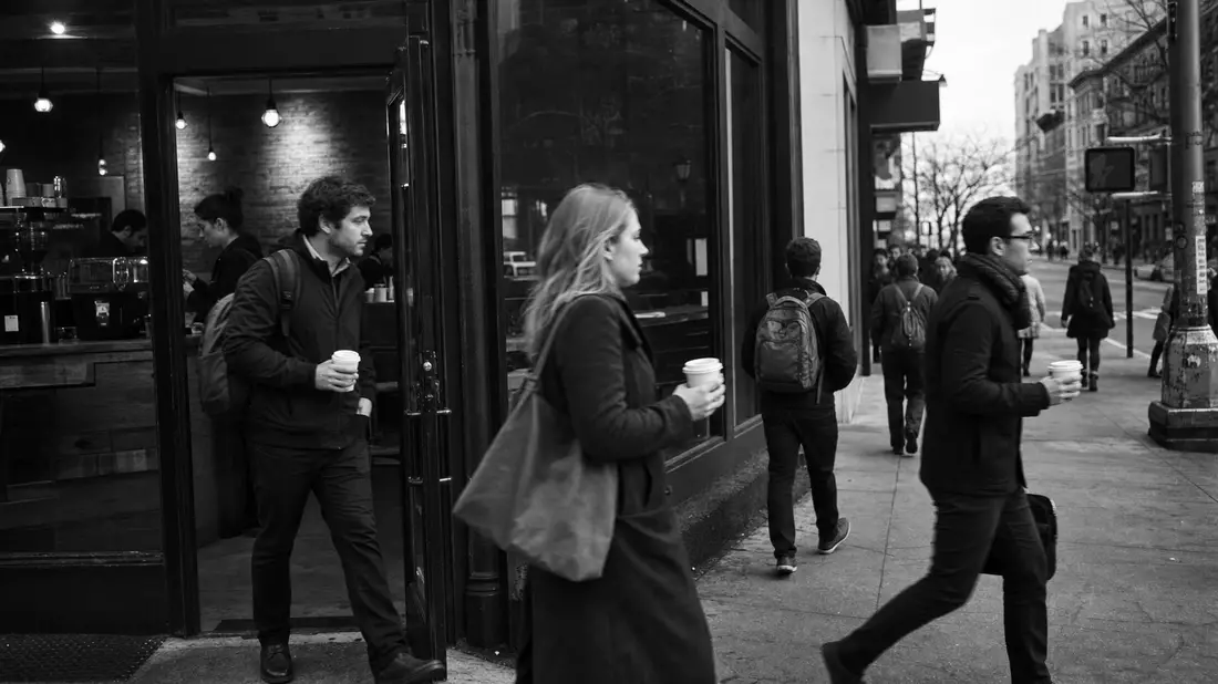 Schwarzweiß-Straßenfotografie von Pendlern mit Kaffeebechern vor Café am Morgen