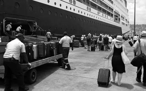 Carnival Corp. Einschiffungshafen im Schwarzweiß-Reportagestil zeigt Gepäck und wartende Passagiere, ISIN US1436583006 - Foto: THN